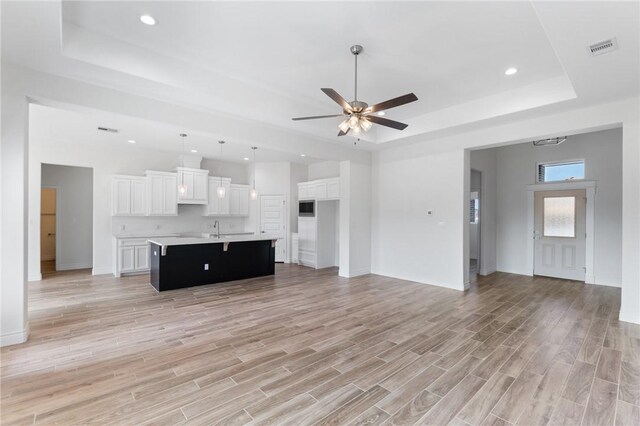 unfurnished living room featuring a tray ceiling, ceiling fan, and sink