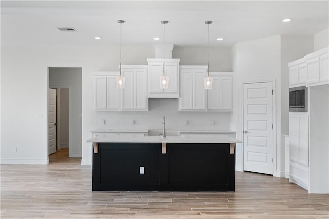 kitchen featuring decorative light fixtures, light stone countertops, white cabinetry, and a kitchen island with sink