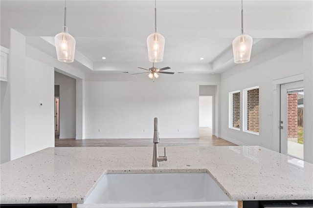 kitchen with a tray ceiling, light stone countertops, sink, and pendant lighting