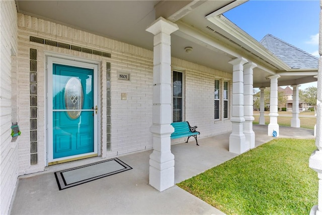 entrance to property featuring a porch, brick siding, and roof with shingles