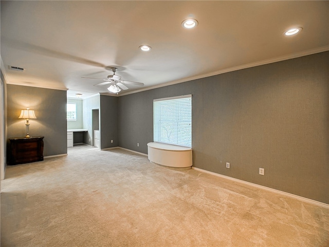 empty room with ceiling fan, light colored carpet, visible vents, baseboards, and ornamental molding