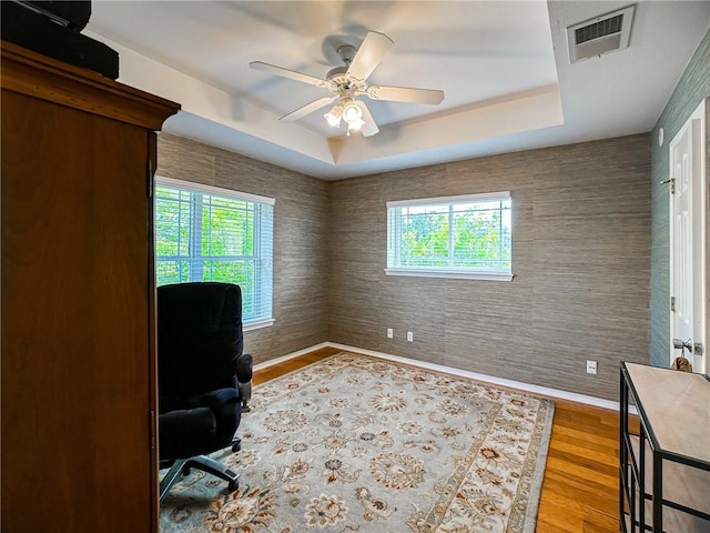 home office featuring light wood finished floors, plenty of natural light, visible vents, and a raised ceiling