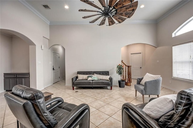 living area featuring arched walkways, light tile patterned flooring, crown molding, and baseboards