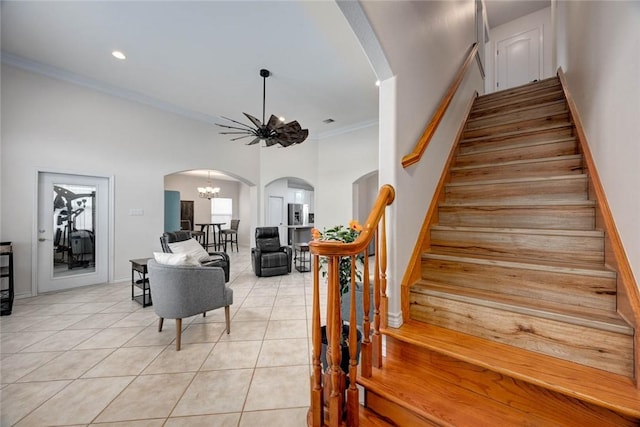 stairs featuring baseboards, arched walkways, tile patterned flooring, crown molding, and a chandelier