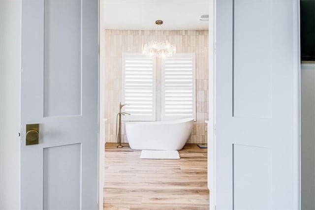 206 Lakeshore St, Port Aransas, TX 78373 - bathroom featuring a chandelier, a freestanding tub, tile walls, and wood finished floors