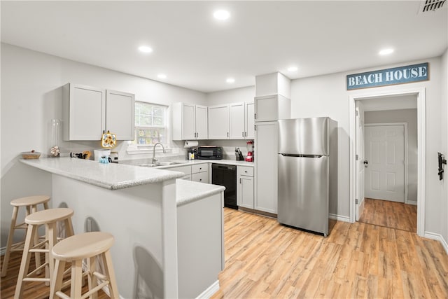 kitchen featuring stainless steel fridge, black dishwasher, a kitchen breakfast bar, white cabinets, and light hardwood / wood-style flooring