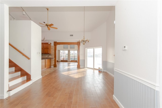 unfurnished living room with ceiling fan with notable chandelier, light hardwood / wood-style floors, and high vaulted ceiling