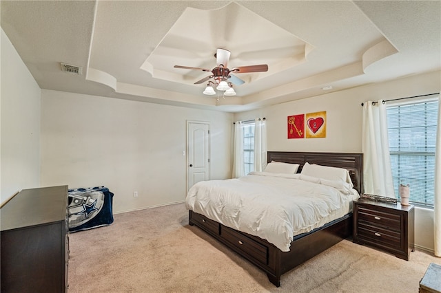 bedroom with a raised ceiling, light carpet, a textured ceiling, and ceiling fan