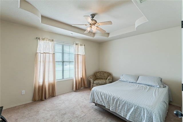 bedroom featuring ceiling fan, a tray ceiling, and light carpet