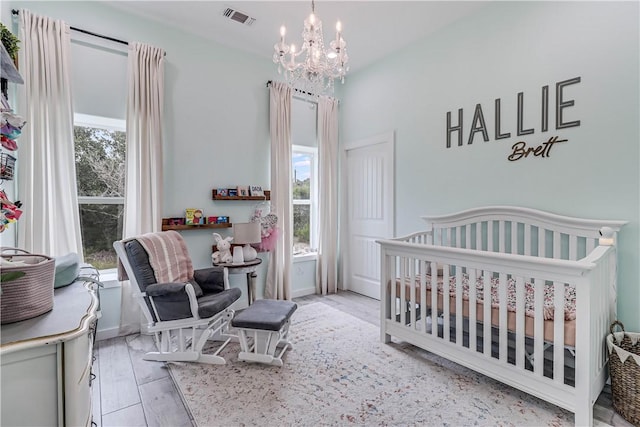 bedroom with a nursery area, a chandelier, light hardwood / wood-style floors, and multiple windows