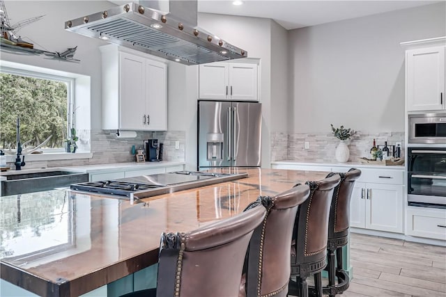 kitchen featuring appliances with stainless steel finishes, white cabinetry, backsplash, island exhaust hood, and light wood-type flooring