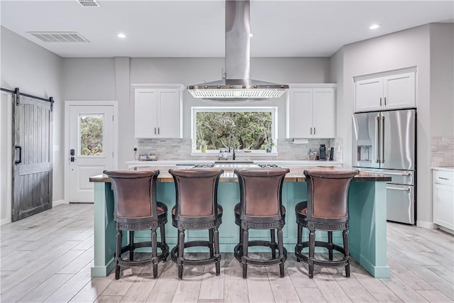 kitchen with high end refrigerator, a barn door, a kitchen island, and white cabinets