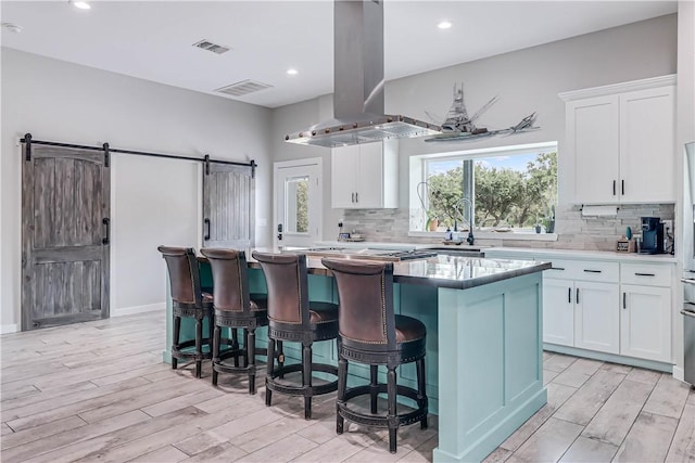 kitchen with a barn door, a center island, island range hood, and white cabinets