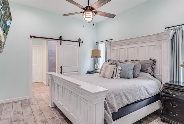 bedroom featuring light hardwood / wood-style floors, a barn door, and ceiling fan