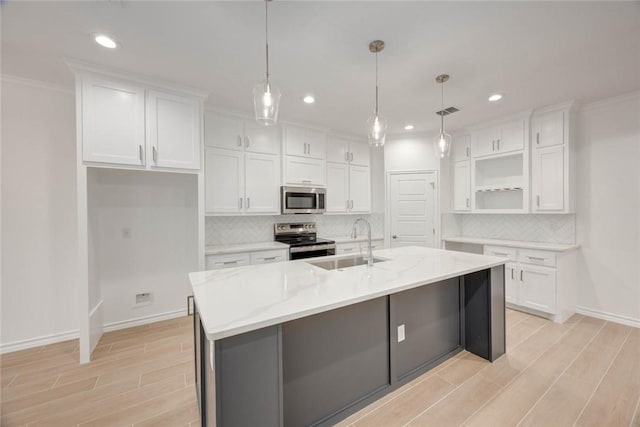 kitchen with a kitchen island with sink, hanging light fixtures, sink, appliances with stainless steel finishes, and white cabinetry