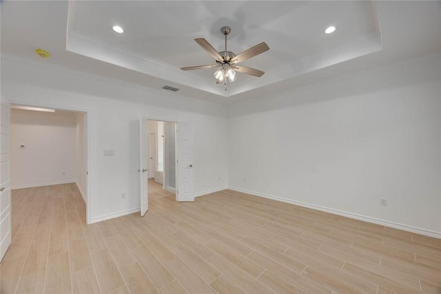 spare room with a tray ceiling, ceiling fan, ornamental molding, and light wood-type flooring