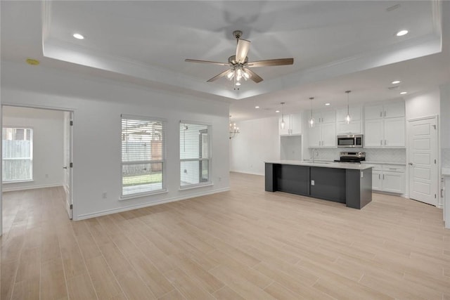 kitchen with white cabinetry, a raised ceiling, pendant lighting, a center island with sink, and appliances with stainless steel finishes