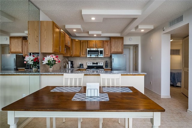 kitchen with visible vents, stone counters, a peninsula, a sink, and appliances with stainless steel finishes