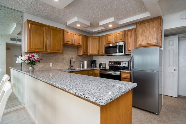 kitchen with light stone counters, brown cabinetry, a peninsula, a sink, and appliances with stainless steel finishes