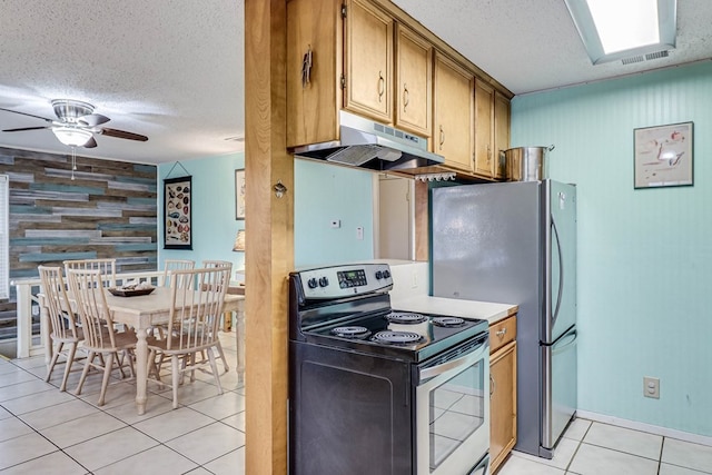 kitchen featuring wooden walls, ceiling fan, light tile patterned floors, a textured ceiling, and appliances with stainless steel finishes