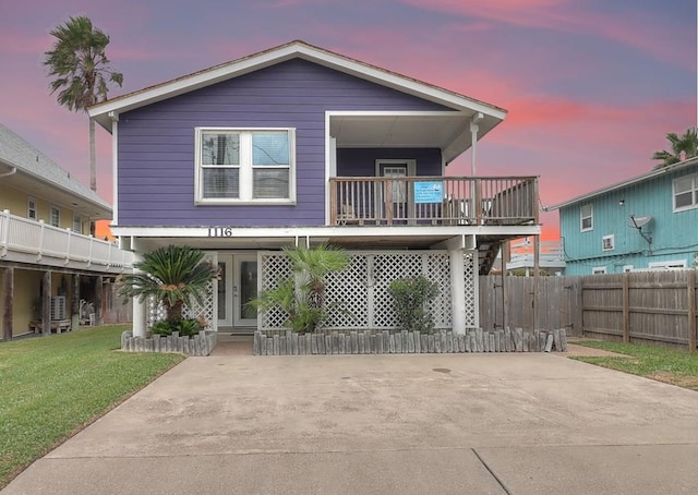 back house at dusk with a yard, french doors, and a balcony