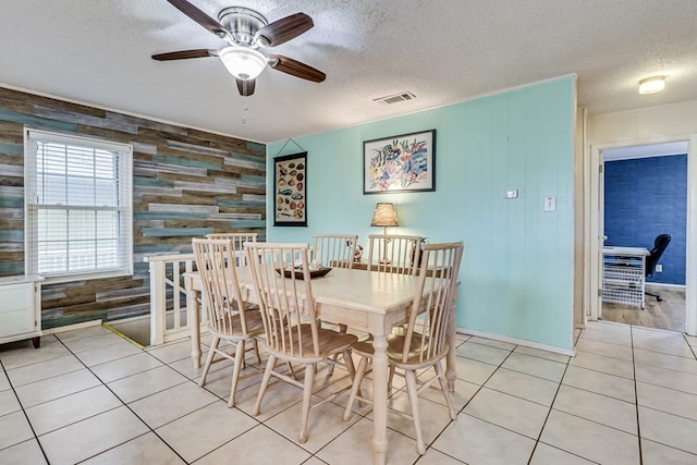 tiled dining area with wood walls, ceiling fan, and a textured ceiling