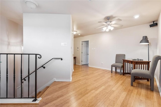 sitting room with light wood-style flooring, a ceiling fan, an upstairs landing, and baseboards