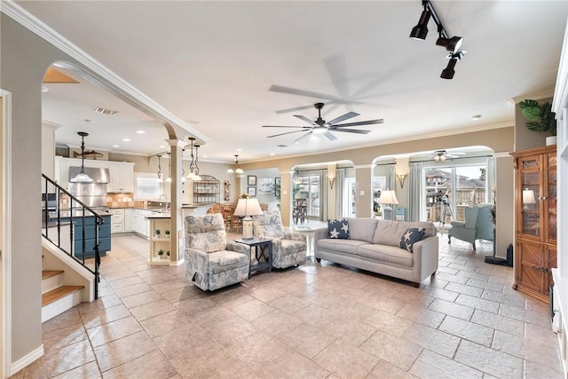 living area with arched walkways, ceiling fan with notable chandelier, visible vents, stairs, and ornamental molding