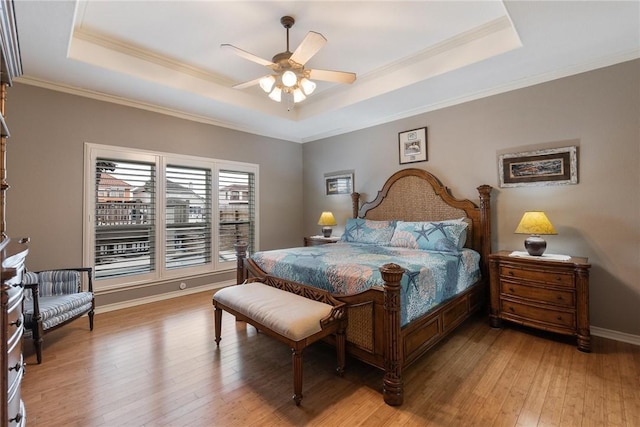 bedroom featuring ornamental molding, a raised ceiling, baseboards, and light wood finished floors