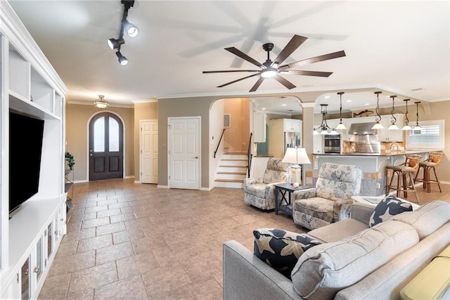 living area with arched walkways, ornamental molding, a ceiling fan, baseboards, and stairs