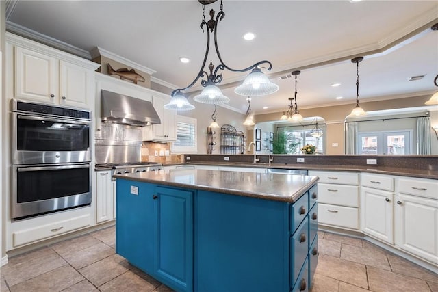 kitchen with appliances with stainless steel finishes, dark countertops, blue cabinets, and wall chimney range hood