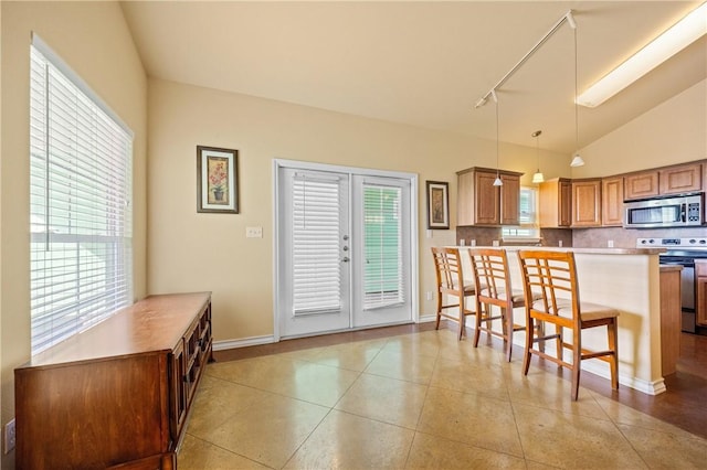 kitchen featuring a breakfast bar area, light tile patterned floors, stainless steel appliances, decorative backsplash, and vaulted ceiling