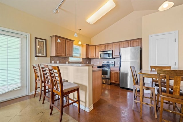 kitchen featuring a peninsula, stainless steel appliances, a kitchen breakfast bar, brown cabinets, and backsplash