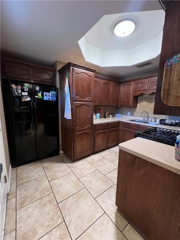 kitchen featuring light tile patterned floors, sink, dark brown cabinetry, black appliances, and a raised ceiling