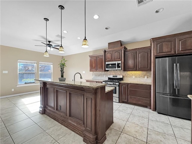 kitchen featuring dark brown cabinetry, light stone counters, backsplash, decorative light fixtures, and appliances with stainless steel finishes