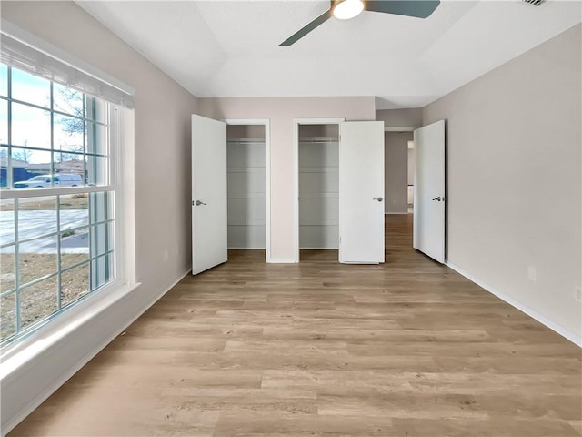 unfurnished bedroom featuring two closets, ceiling fan, and light hardwood / wood-style floors