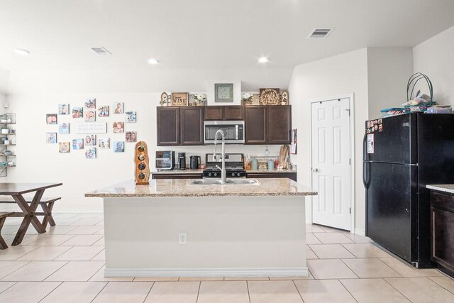 kitchen with a kitchen island with sink, light tile patterned flooring, light stone counters, and appliances with stainless steel finishes