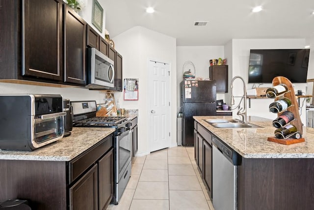 3906 Targaryen Way, Corpus Christi, TX 78410 - kitchen with stainless steel appliances, dark brown cabinets, light tile patterned floors, a kitchen island with sink, and light stone counters