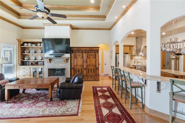 living area with light wood-style floors, a fireplace, a high ceiling, and crown molding