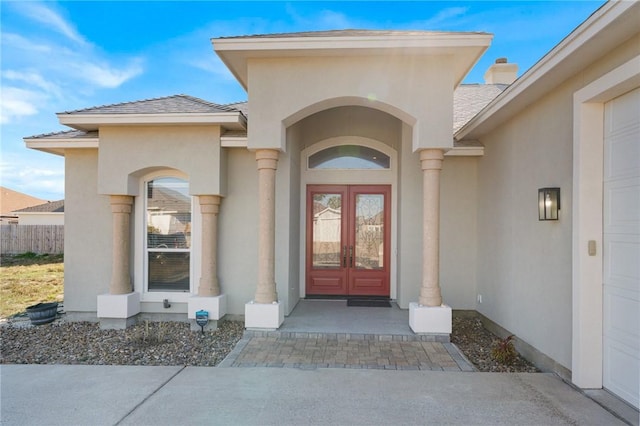 entrance to property with french doors, fence, an attached garage, and stucco siding