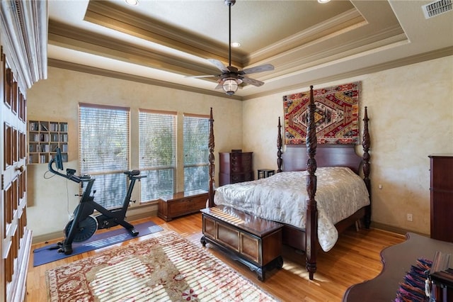 bedroom with light wood-style floors, a raised ceiling, and visible vents