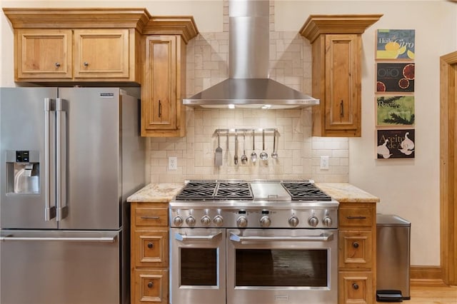 kitchen featuring appliances with stainless steel finishes, decorative backsplash, light stone counters, and wall chimney exhaust hood