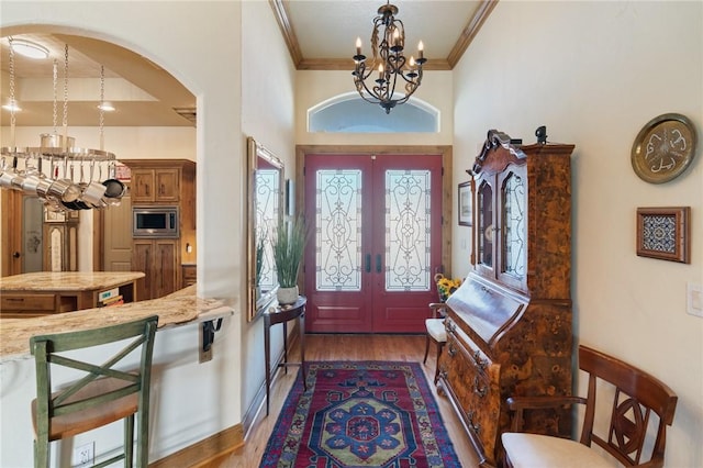 entrance foyer with arched walkways, a notable chandelier, wood finished floors, french doors, and ornamental molding