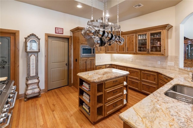 kitchen featuring arched walkways, brown cabinets, stainless steel appliances, visible vents, and light wood-style floors