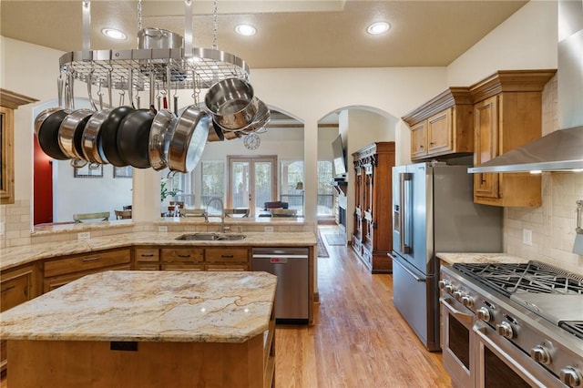 kitchen featuring stainless steel appliances, brown cabinets, a sink, and wall chimney exhaust hood