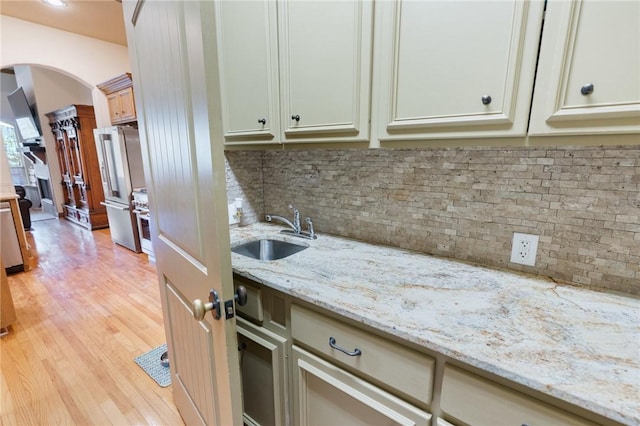 kitchen featuring light wood finished floors, arched walkways, a sink, stainless steel appliances, and backsplash