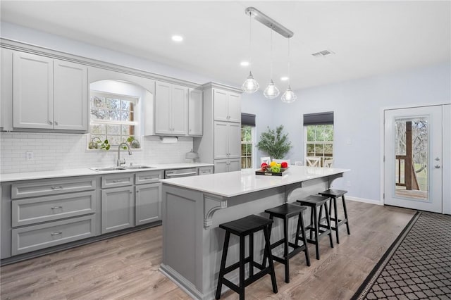 kitchen with sink, gray cabinetry, a kitchen breakfast bar, a center island, and decorative light fixtures