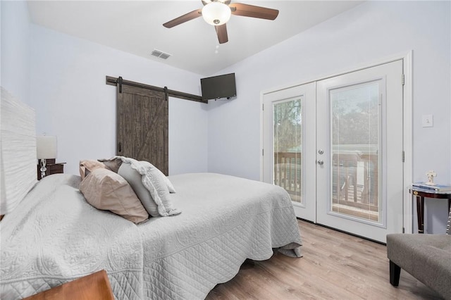 bedroom with french doors, light hardwood / wood-style flooring, access to outside, ceiling fan, and a barn door