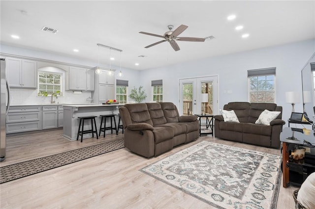 living room featuring sink, light hardwood / wood-style floors, french doors, and ceiling fan