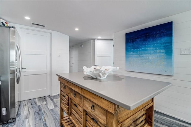 kitchen featuring light countertops, visible vents, brown cabinetry, freestanding refrigerator, and a kitchen island